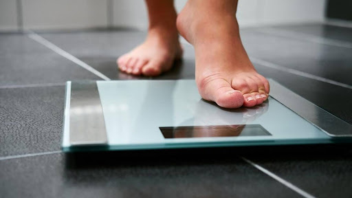 Person struggling with weight loss despite dieting showing frustration on weighing scale