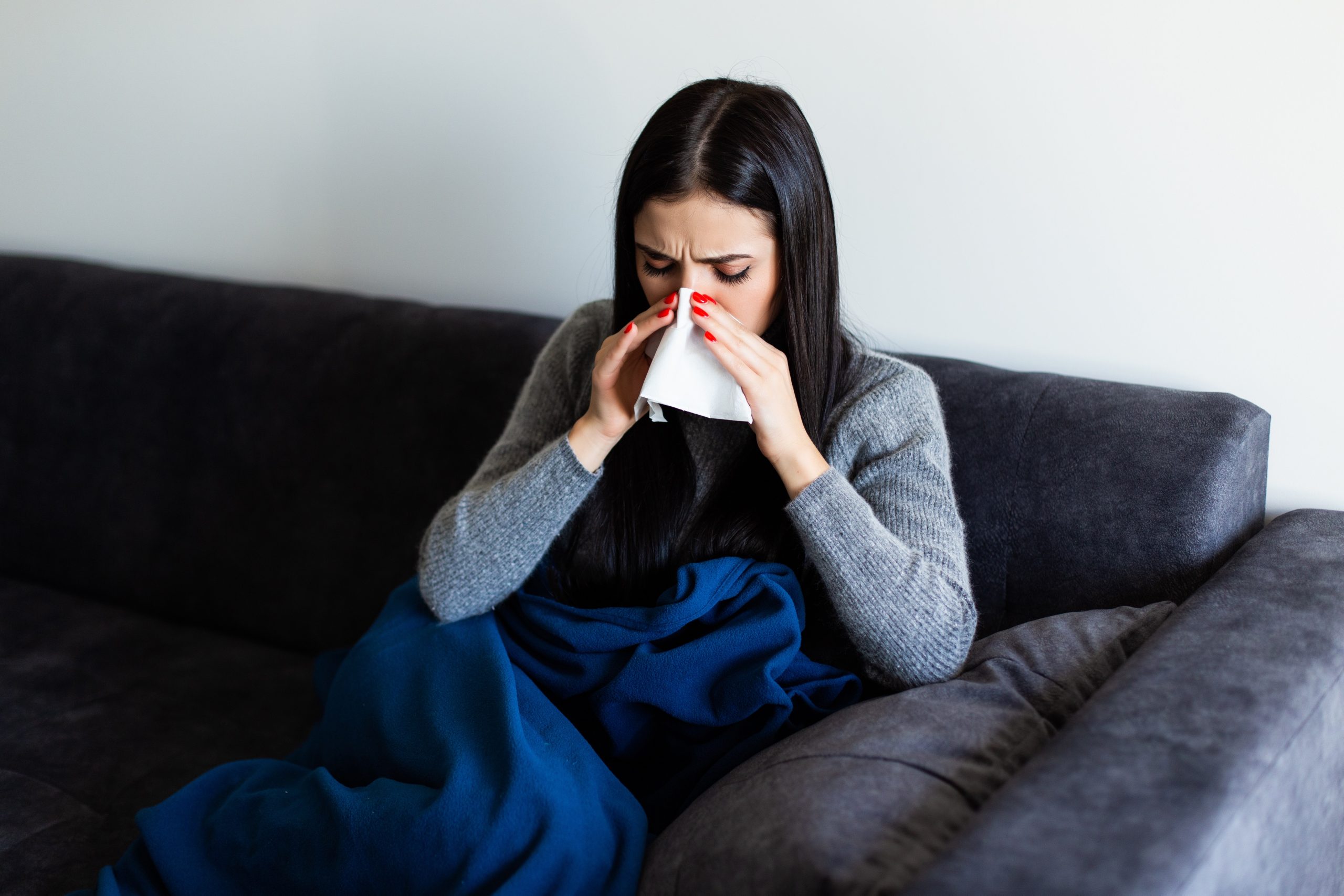 Sick woman sitting on sofa blowing her nose at home in the sitting room
